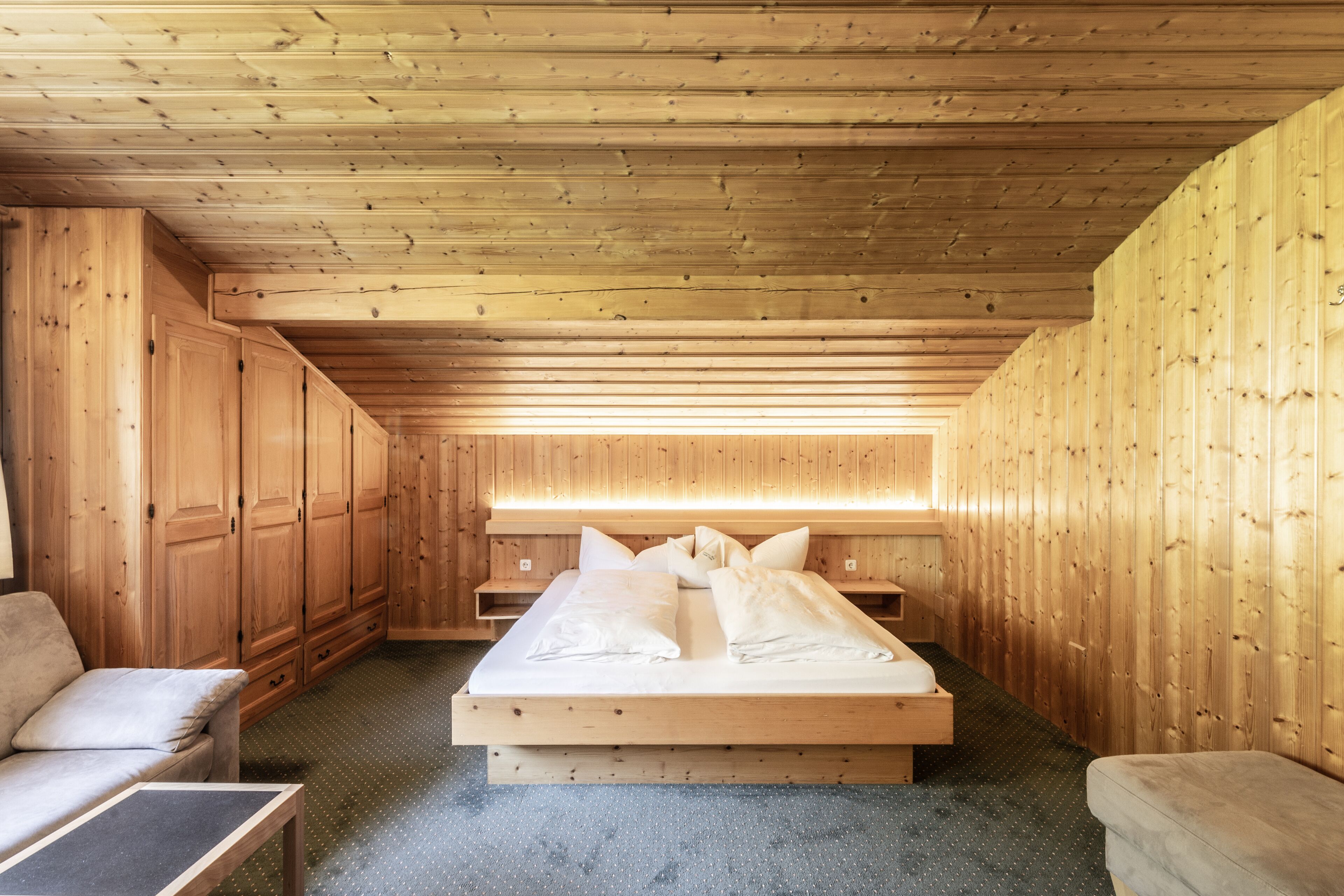 A wooden cabin bedroom with a bed, a sofa, and built-in wooden cabinets.