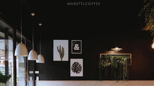 A modern coffee shop interior with a brick wall, hanging plants, and minimalist furniture. - Marktel&Coffee - Hostel (Chiang Mai)