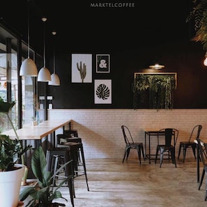 Ein modernes Café-Interieur mit Backsteinwand, hängenden Pflanzen und schlichter Einrichtung.