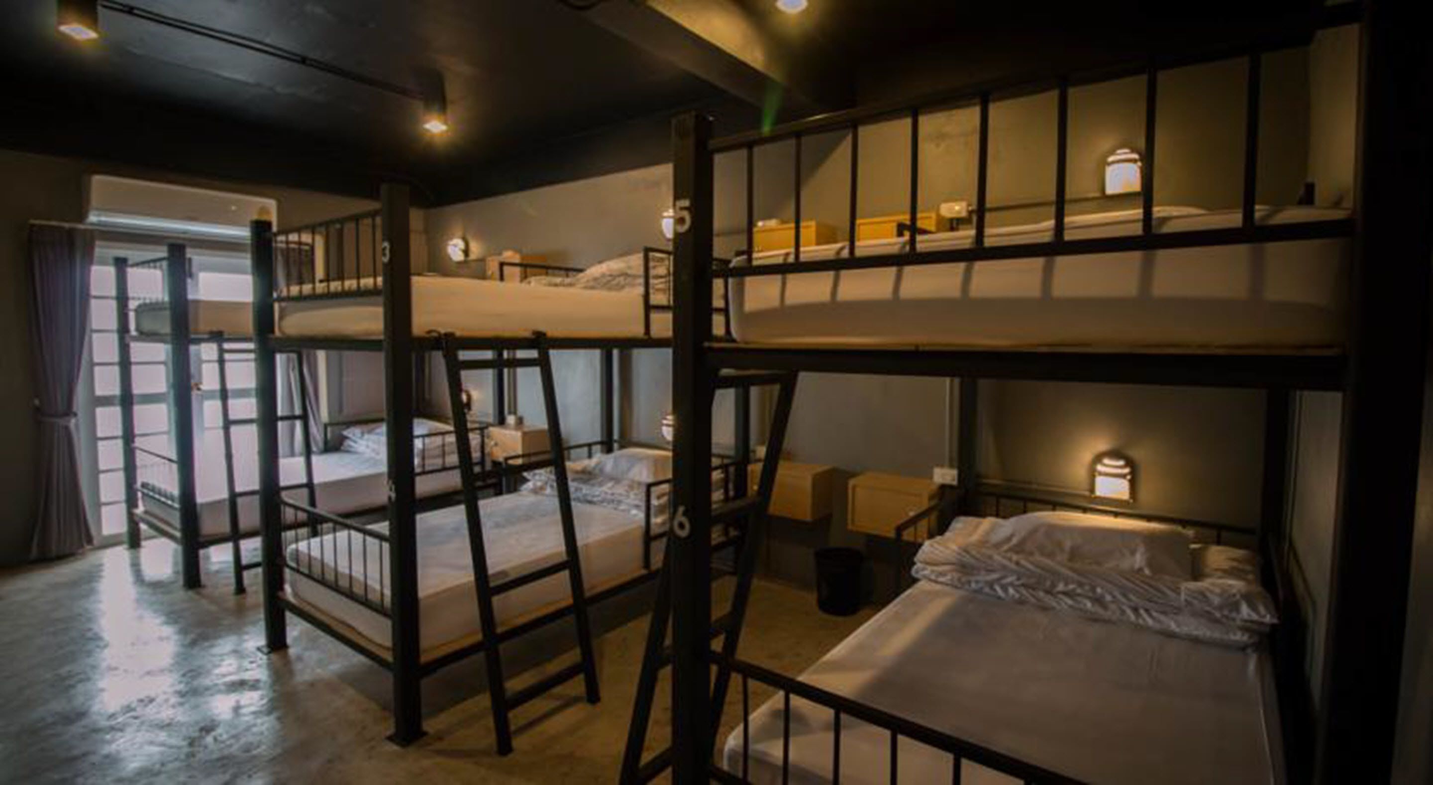 A bunk bed room with multiple beds, each with a small table and a lamp.