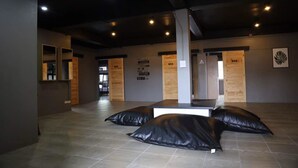 A spacious room with a high ceiling and recessed lighting. There are two black cushions on the floor and a wooden bench in the center. - Marktel&Coffee - Hostel (Chiang Mai)