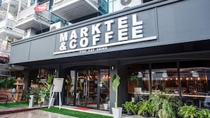 A modern coffee shop named 'MARKTEL & COFFEE' with a glass facade, outdoor seating, and a small garden area. - Marktel&Coffee - Hostel (Chiang Mai)