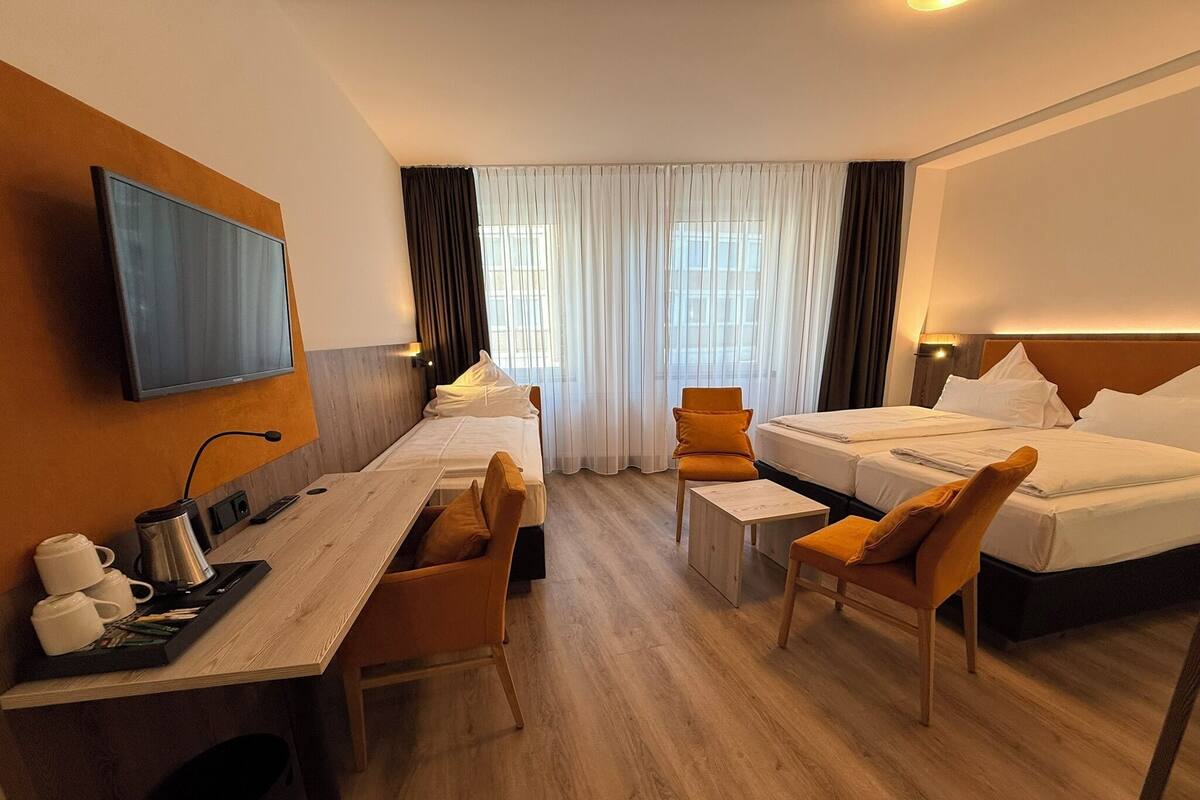 Habitación de hotel con dos camas, un escritorio con cafetera, una silla y un televisor montado en la pared.