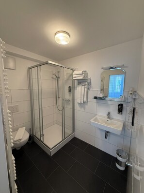 A modern bathroom with a glass shower enclosure, a white sink, a mirror, and a toilet. - Minx - CityHotels (Aachen)