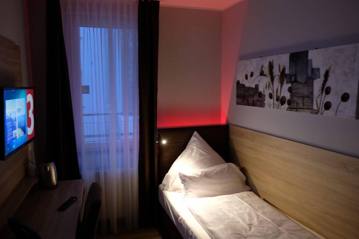 Una habitación de hotel con cama, televisor, escritorio y ventana con cortinas.