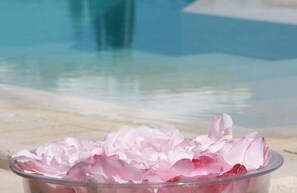 Vista despejada de una piscina con barrera de vidrio y un recipiente con pétalos rosas en primer plano.