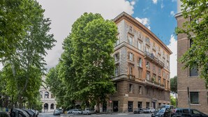 A multi-story building with a classical architectural style, featuring a prominent entrance with an archway, multiple balconies, and a mix of window styles. - Colosseum Corner (Rome)