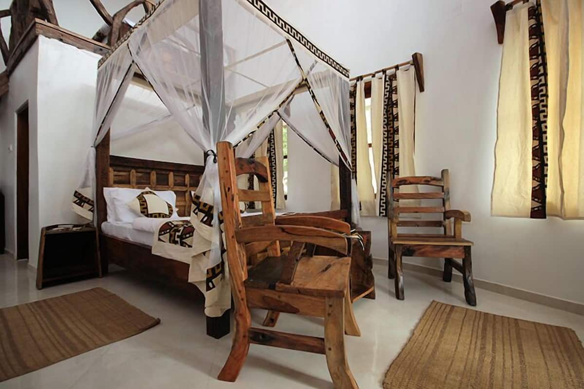 A bedroom with a four-poster bed, wooden chairs, and a small bedside table.