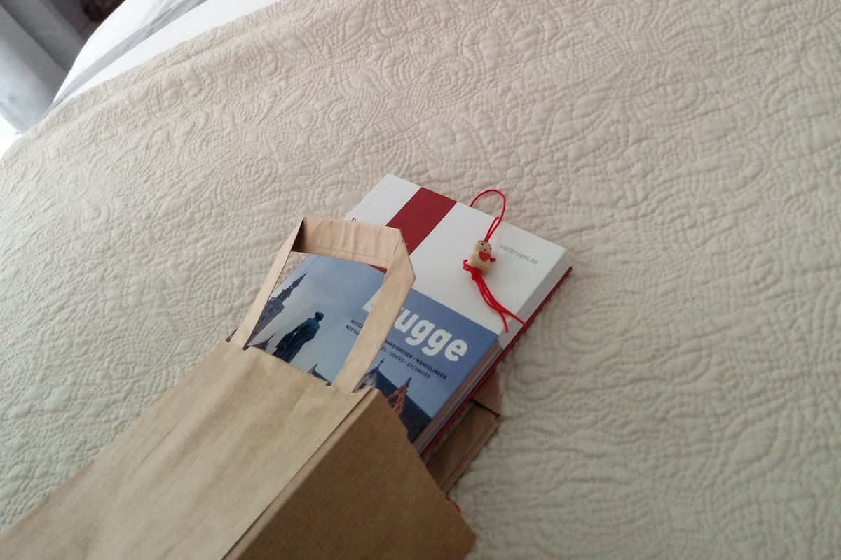 A bed with a white quilt, a pink pillow, and a polka dot pillow. There is a small wooden box and a book on the bed.