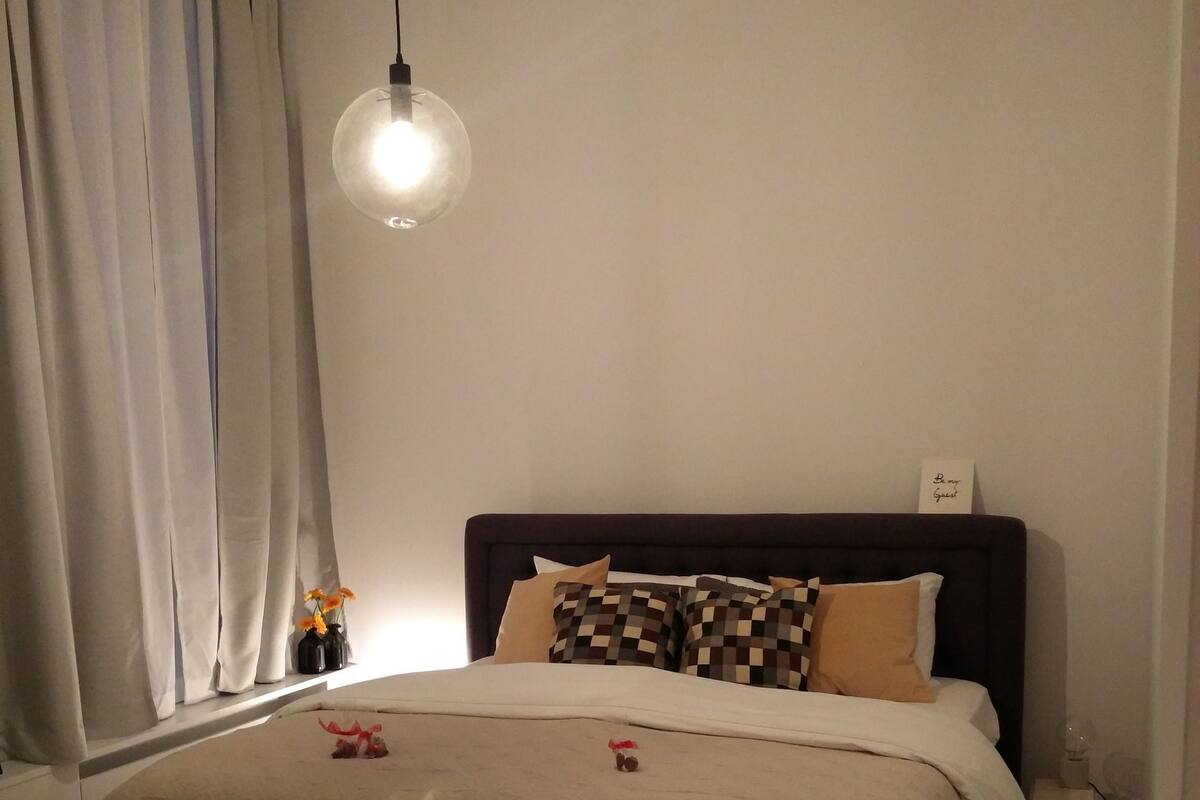 A neatly made bed with a patterned headboard, a bedside table with a lamp, and a window with curtains.