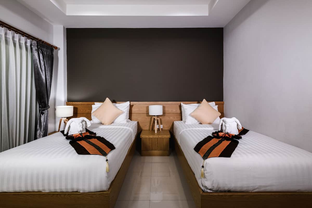 Een hotelkamer met twee bedden, een donkere accentmuur en een groot raam met gordijnen.