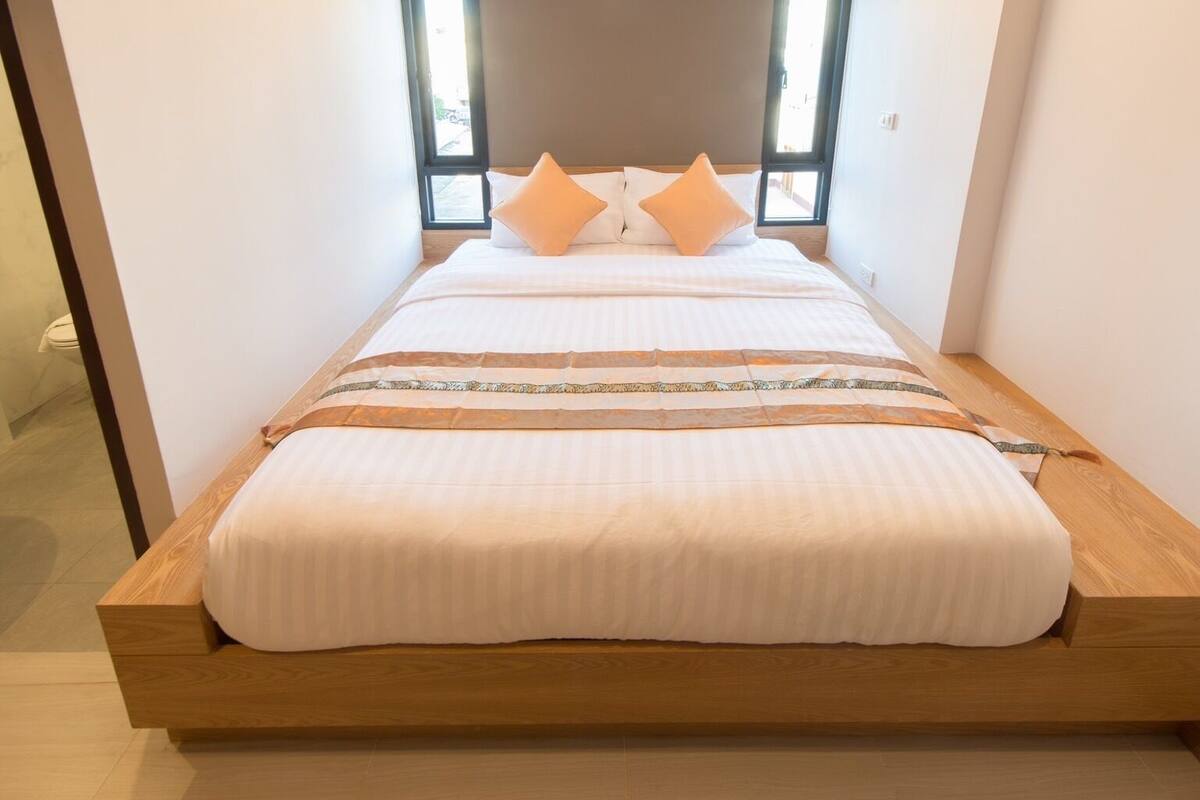 Een bed met houten frame, witte beddengoed en twee oranje kussens.