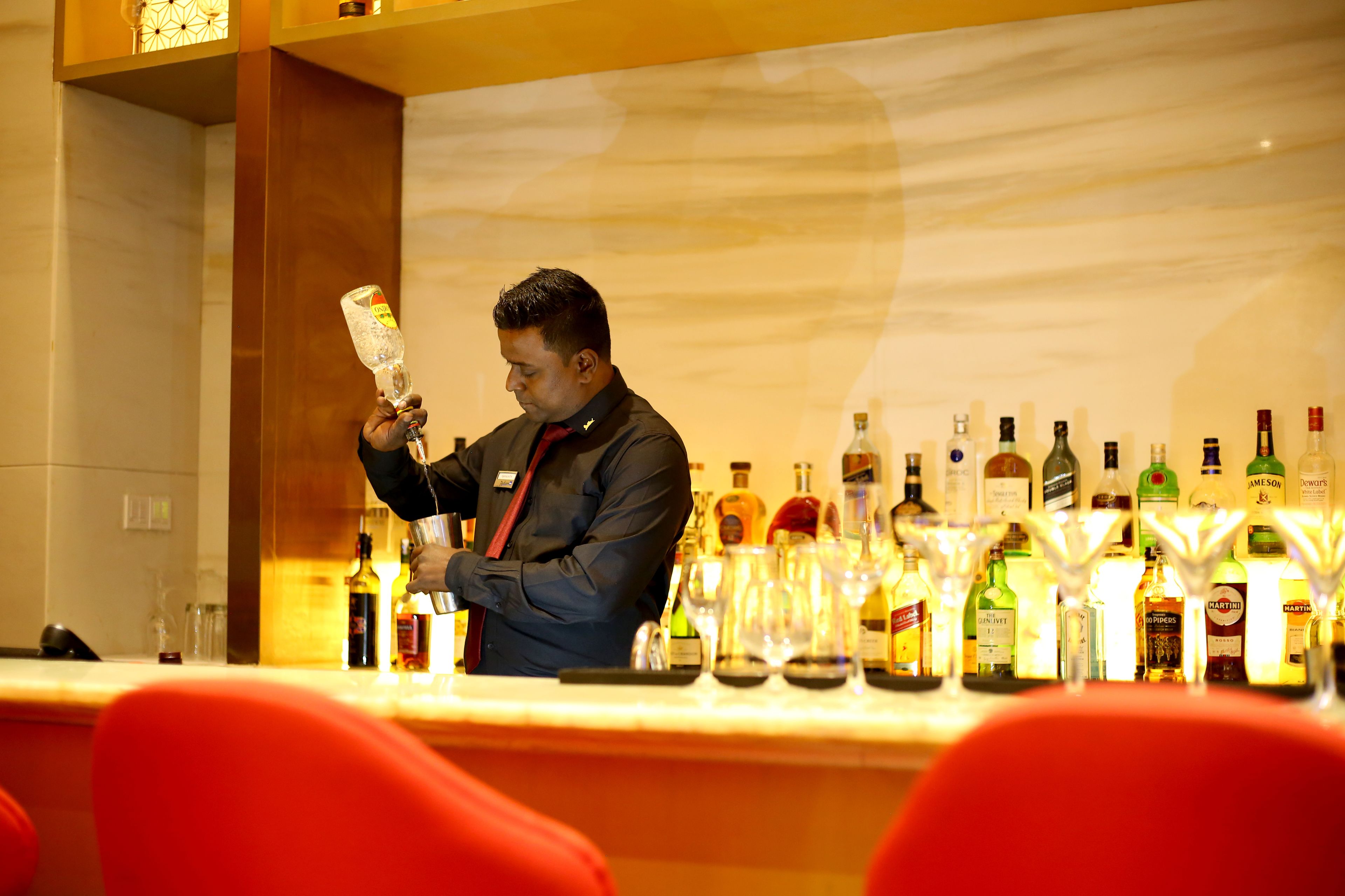 Un espace bar où un barman prépare une boisson, entouré de différentes bouteilles et de verres.