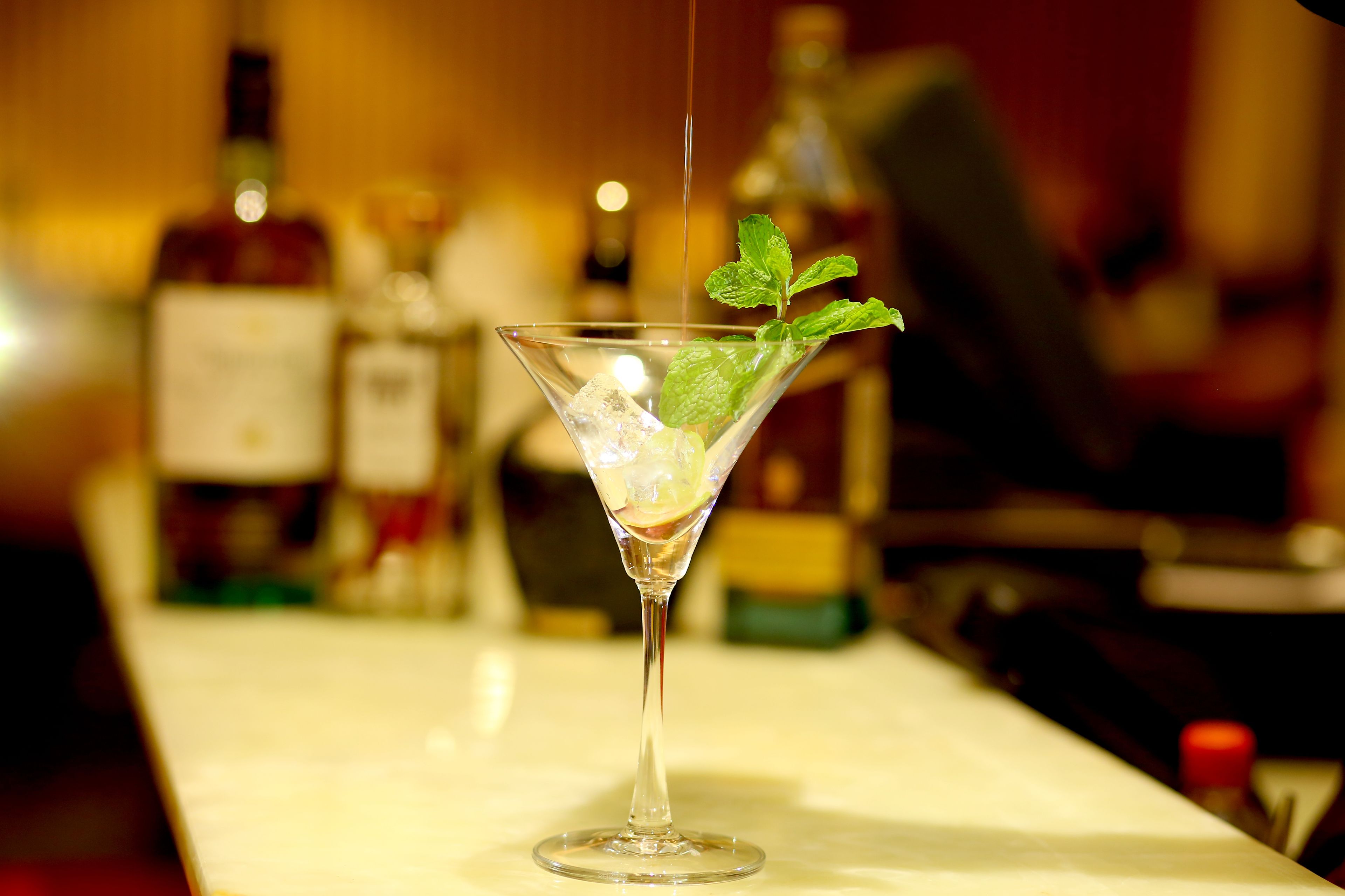 A martini glass with mint leaves and ice cubes on a bar counter.