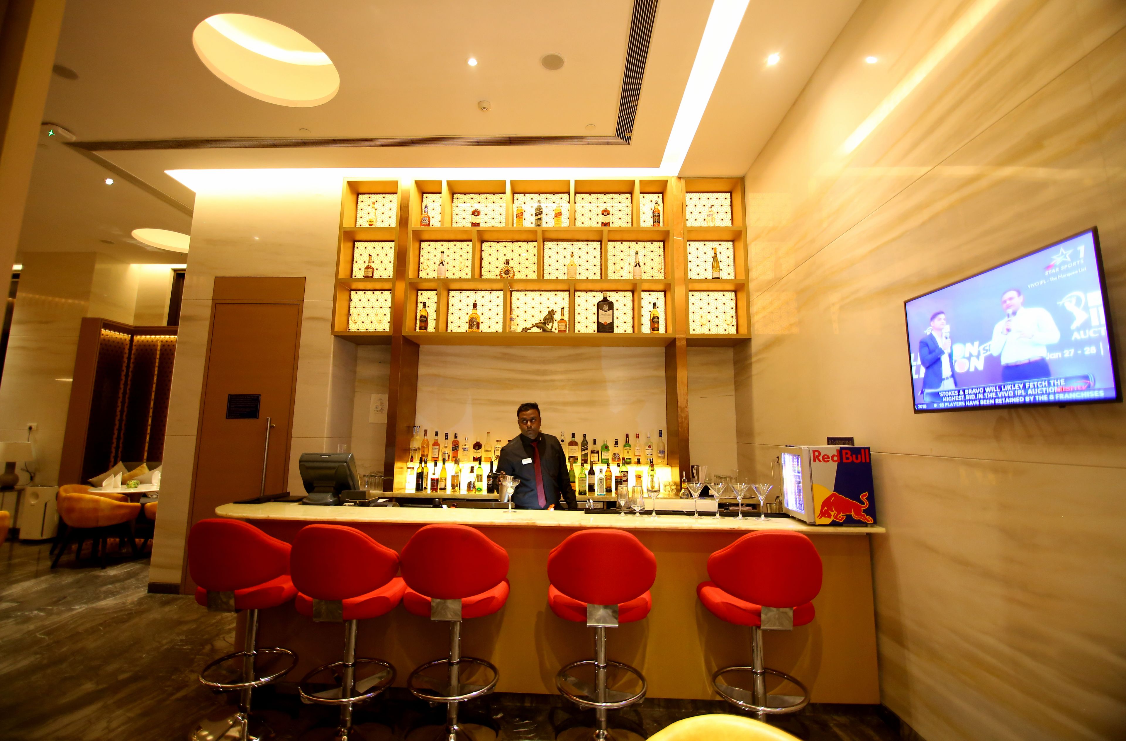 A bar area with a bartender, red bar stools, a television screen, and a Red Bull advertisement.
