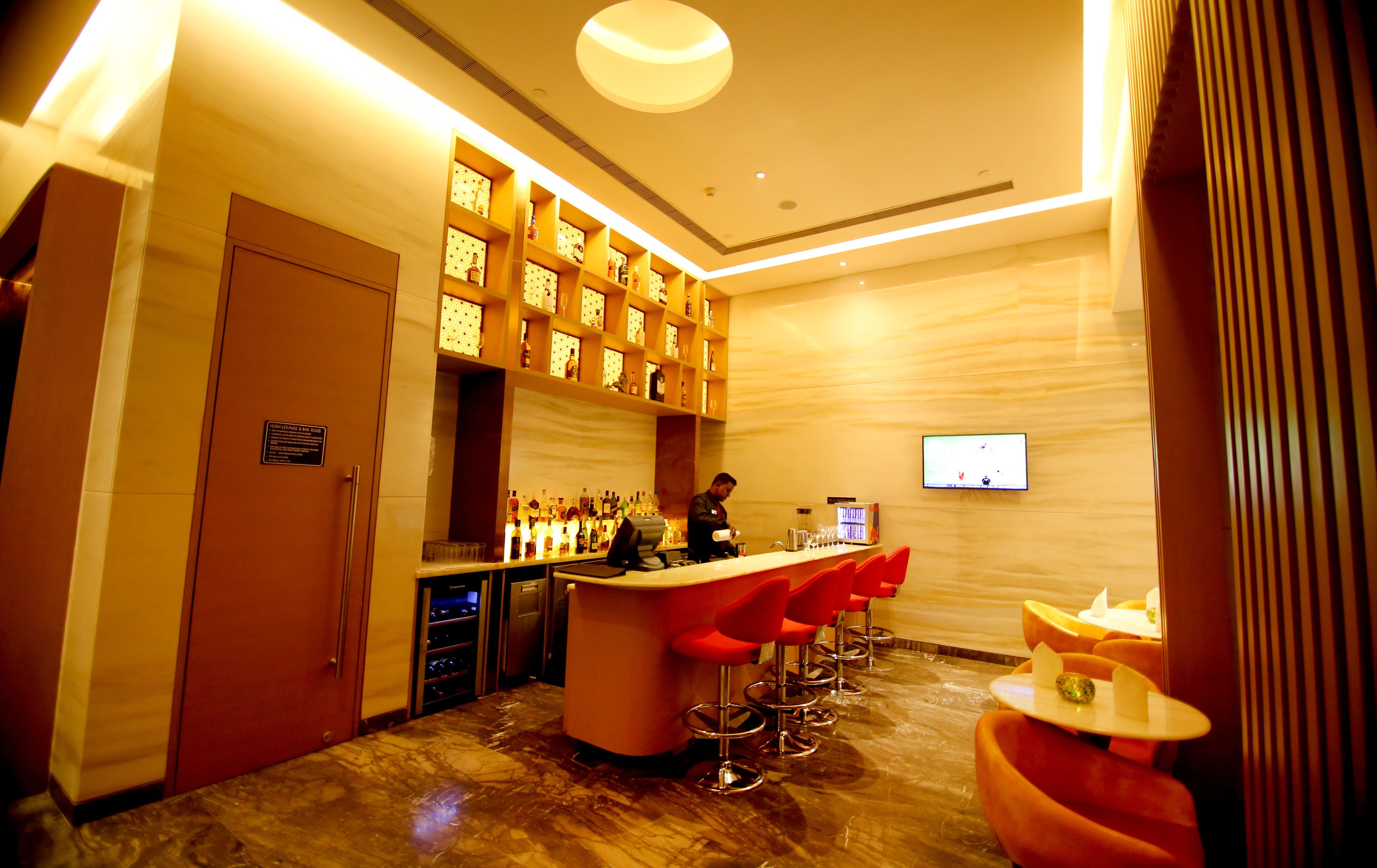 A bar area with a bartender, red bar stools, and shelves of bottles.