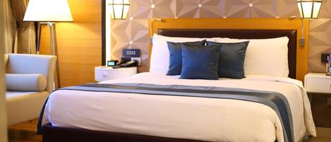 Una habitación de hotel con una cama grande, una mesita de noche, una lámpara y una silla.