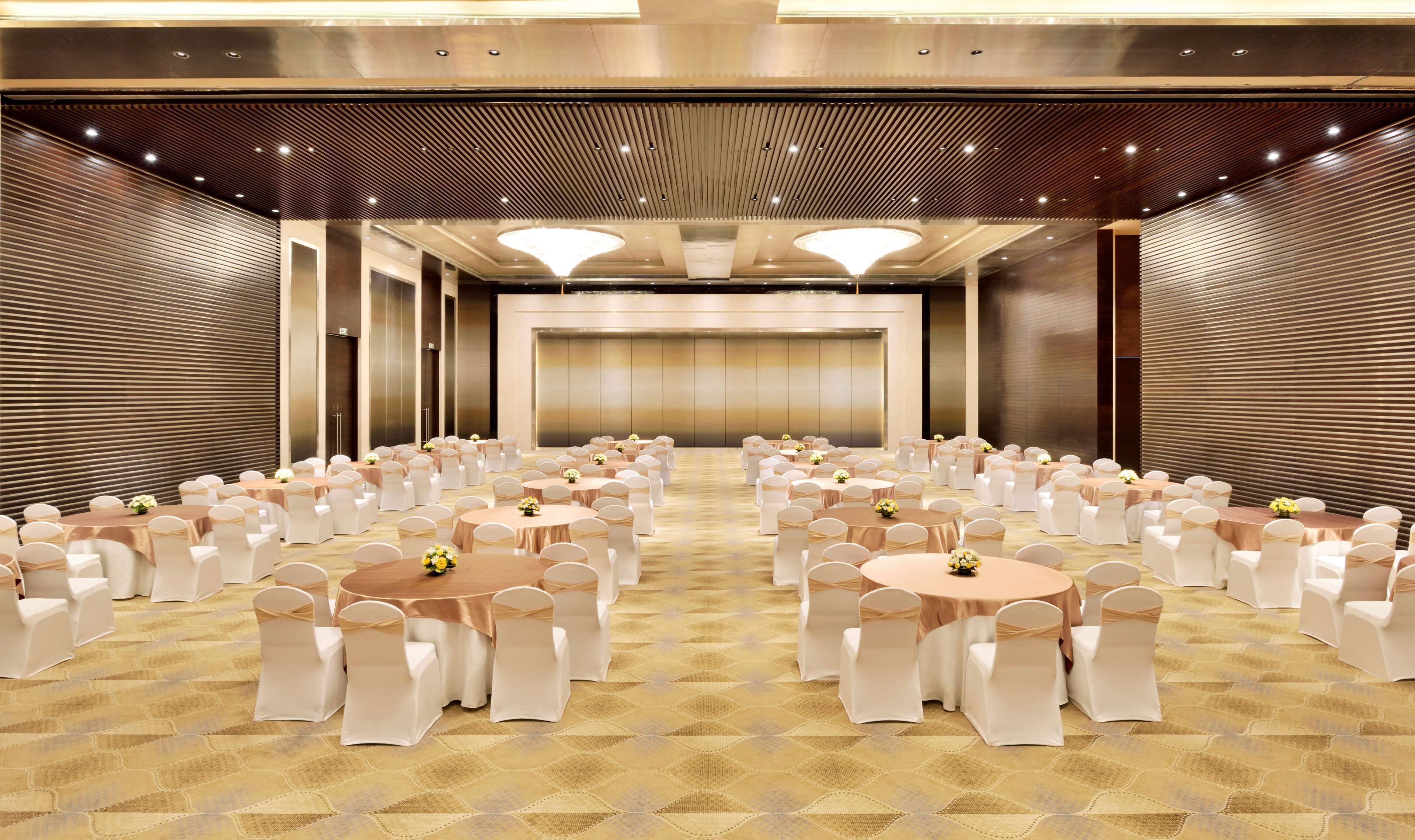 A large conference room with multiple round tables and white chairs, arranged in rows.