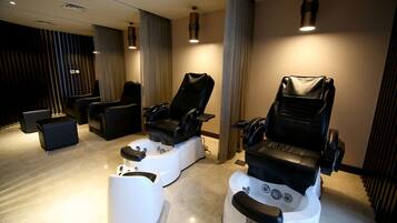 A spa room with two massage chairs, a white foot bath, and a small table.
