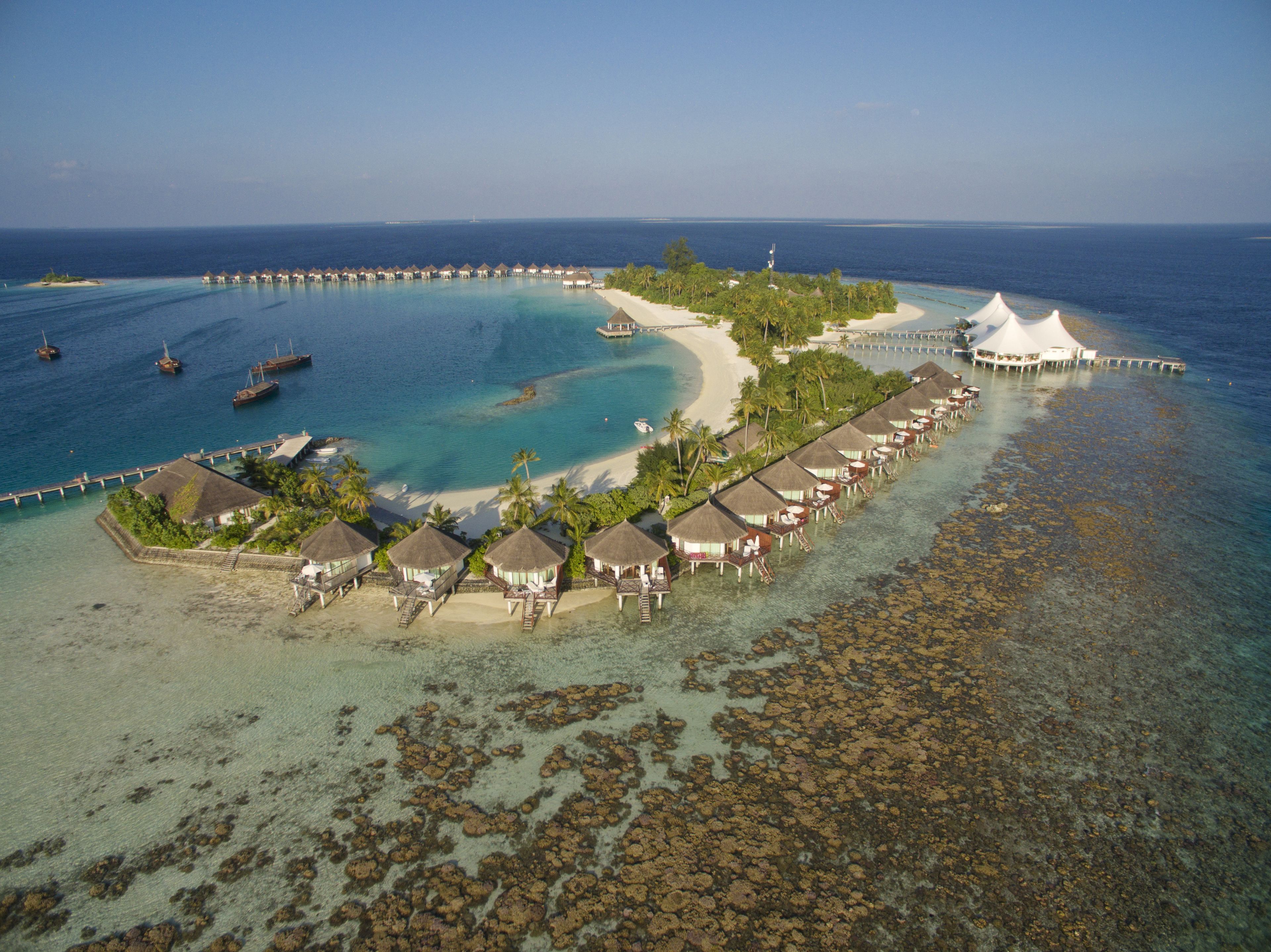An overwater bungalows resort with clear blue waters, a sandy beach, and a pier extending into the sea.