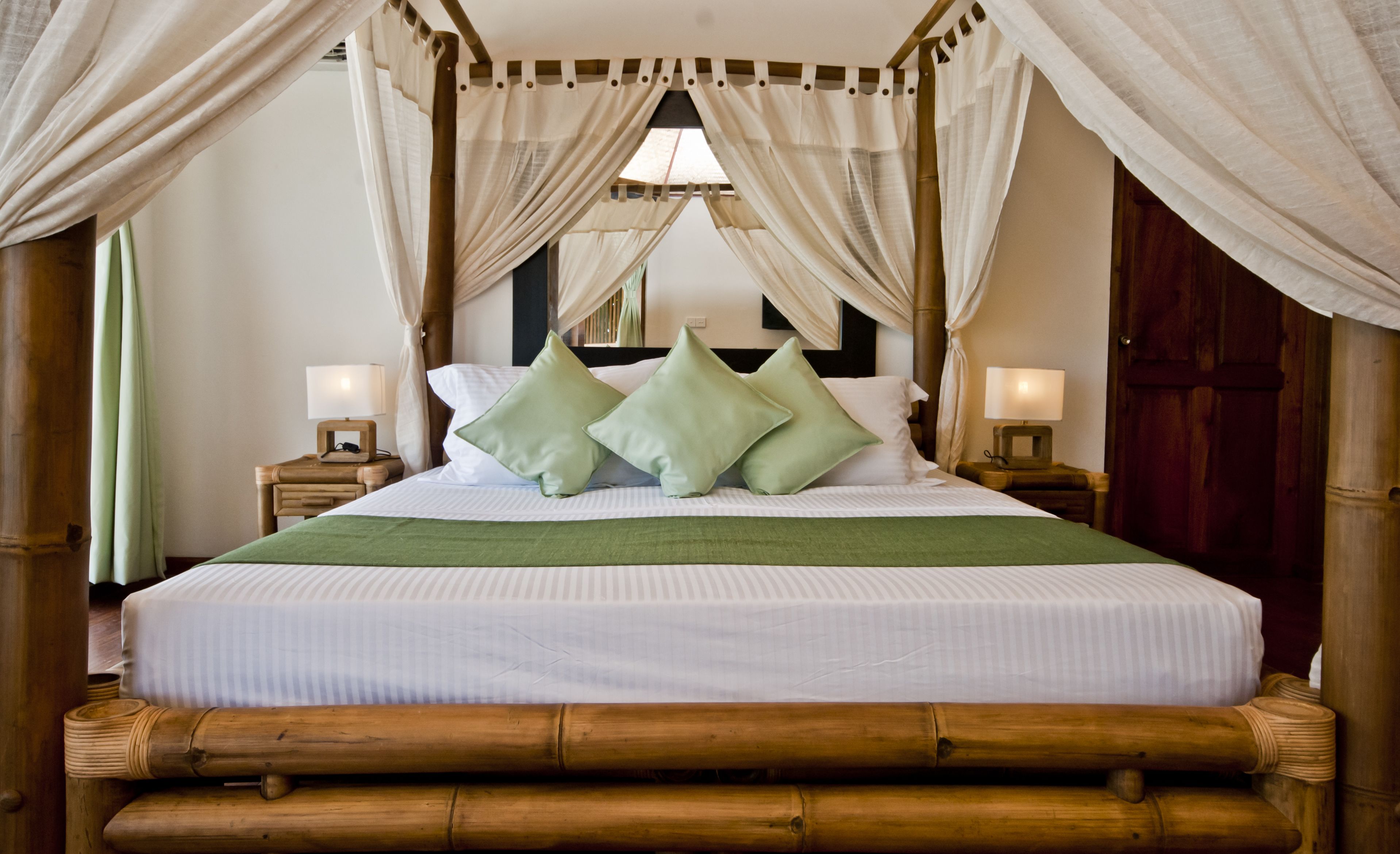 Una habitación con una cama, dos mesitas de noche, una manta verde y un cabecero de madera.