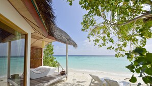 A beachside room with a thatched roof, a wooden deck, and a view of the ocean. - Safari Island Resort (Mushimasgali)