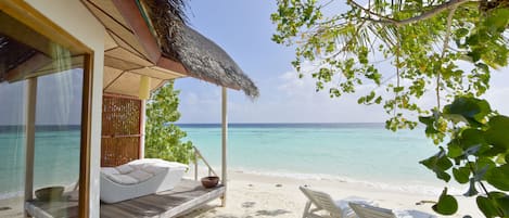 Una habitación frente a la playa con techo de paja, terraza de madera y vista al océano.