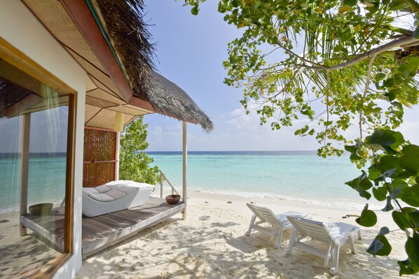 A beachside room with a thatched roof, a wooden deck, and a view of the ocean. - Safari Island Resort (Mushimasgali)