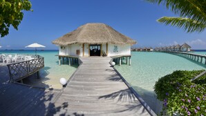 A wooden pier leading to a thatched-roof overwater bungalow with a pool and lounge chairs. - Safari Island Resort (Mushimasgali)