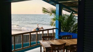 Un restaurant en bord de mer offrant une vue sur l’océan, avec des tables et des chaises en bois, et un toit de chaume.
