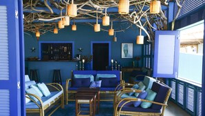 Une pièce aux tons bleus, avec des meubles en osier, un coin bar et des luminaires suspendus.