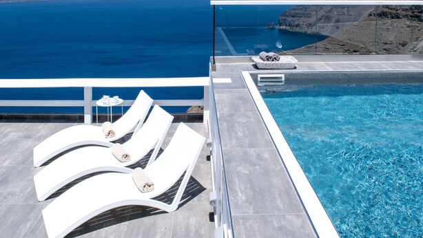 A poolside area with lounge chairs and a view of the sea. - Thireas Hotel (Santorini)