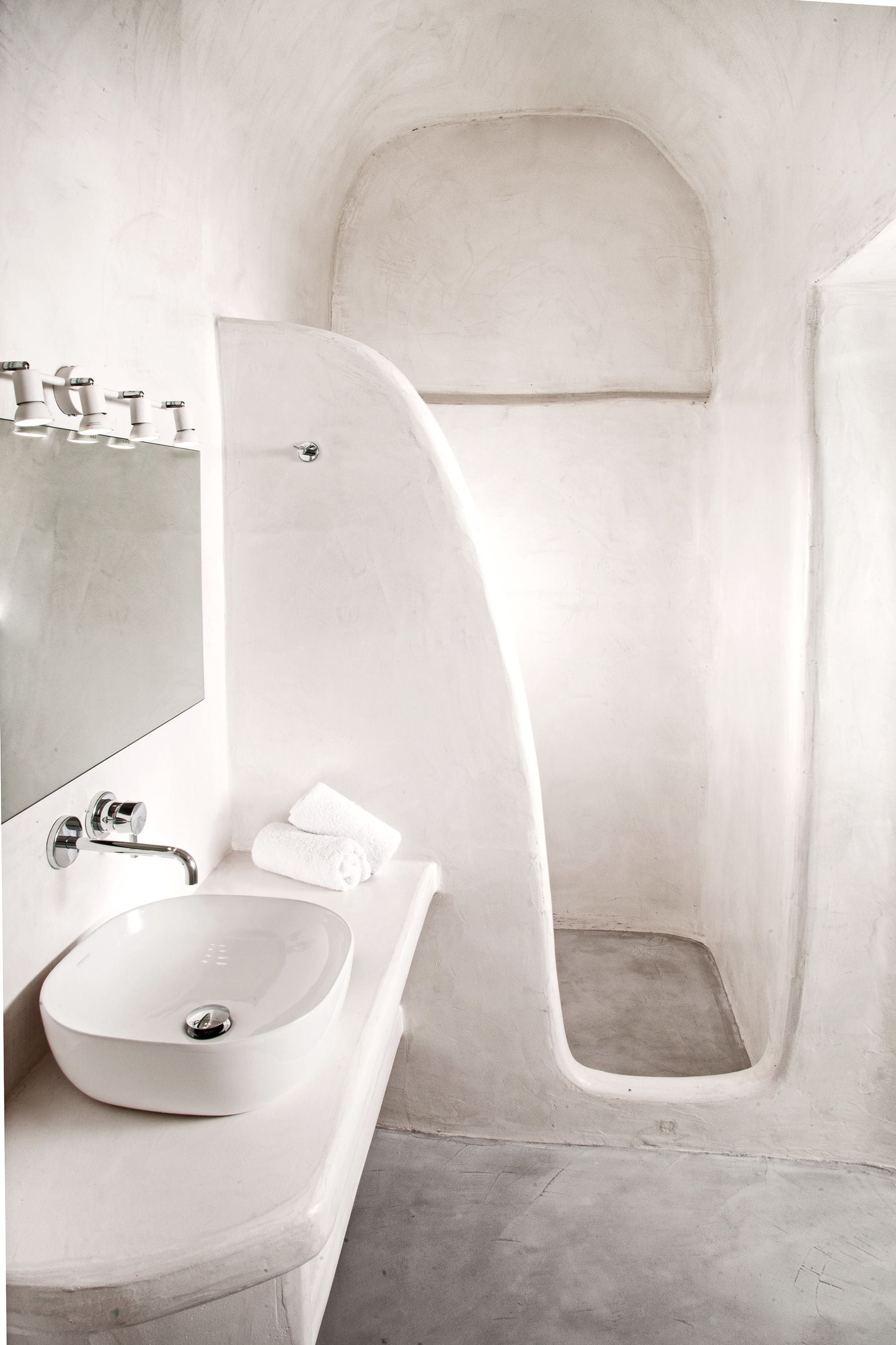 A modern bathroom with a white sink, a mirror, and a shower area.