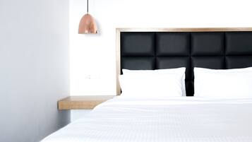 Un dormitorio moderno con una cama, una mesita de noche de madera, un cabecero tapizado negro y una lámpara colgante.
