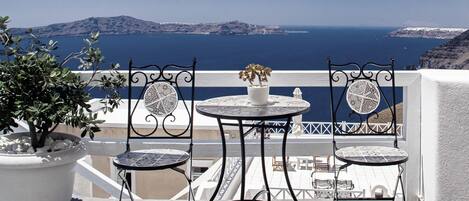 A terrace with a table and two chairs, a potted plant, and a view of the sea and islands.
