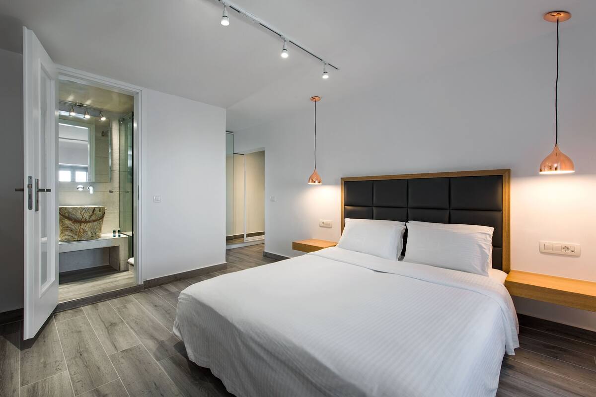 A modern bedroom with a large bed, a walk-in closet, and pendant lighting.