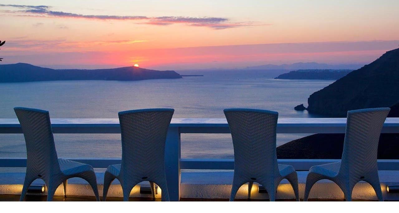 Une vue sur le coucher de soleil depuis un balcon agrémenté de chaises en osier et d’une balustrade.