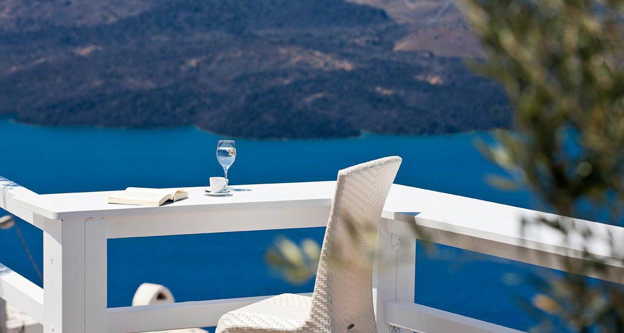 Un área de estar exterior blanca con vistas a una masa de agua azul y montañas.