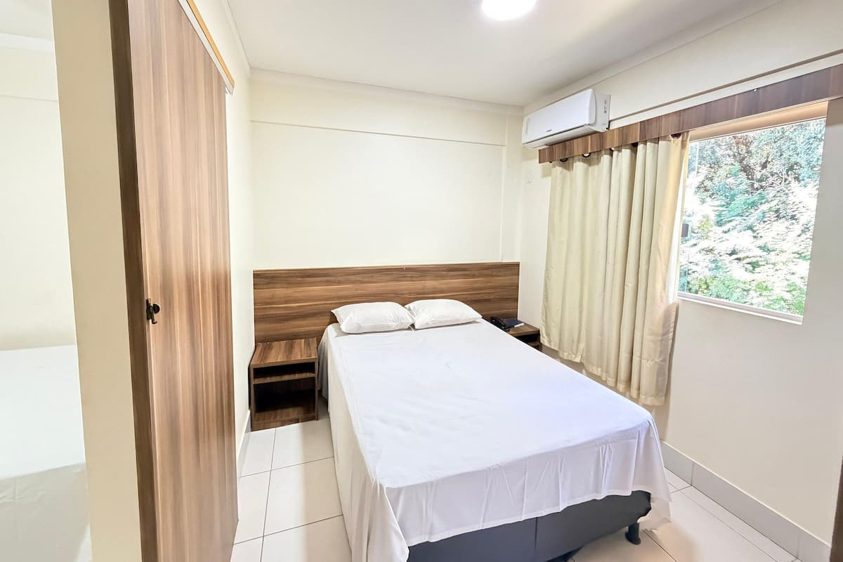 A hotel room with a bed, bedside table, and an air conditioning unit.