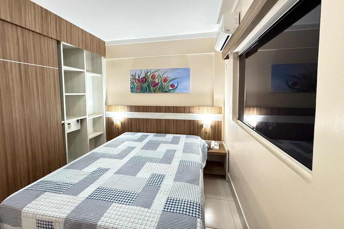 A bedroom with a bed, a painting of flowers, a wardrobe, and a window.