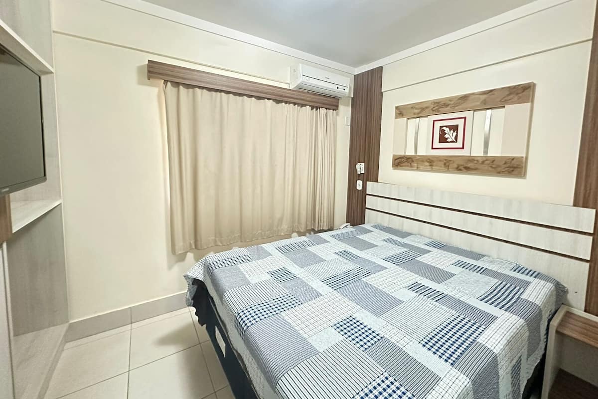A bedroom with a bed, curtains, a mounted TV, and a framed picture on the wall.