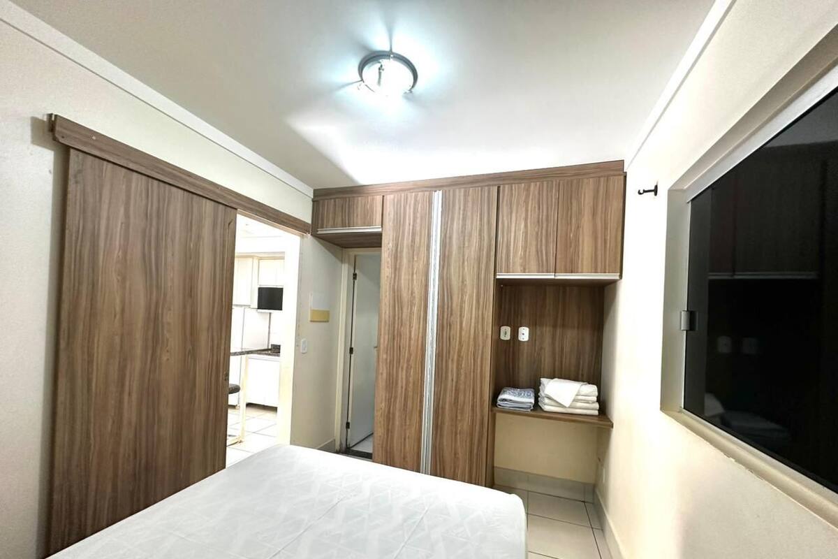 A bedroom with a bed, wardrobe, and a small shelf with towels.
