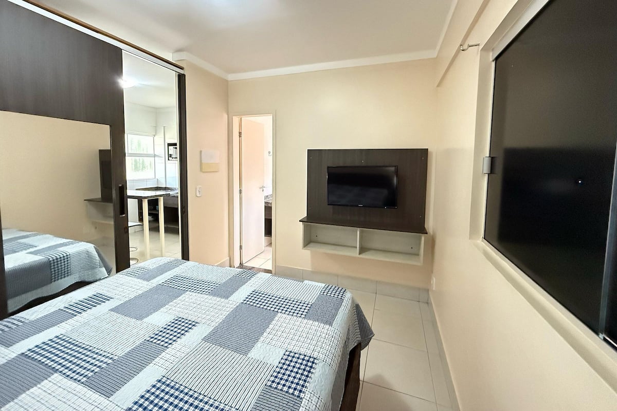 A bedroom with a bed, a TV mounted on the wall, a mirror, and a door leading to a bathroom.