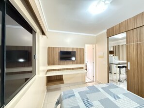 Un dormitori amb televisió penjada a la paret, un llit amb edredó estampat i una porta corredissa que dona a un bany.