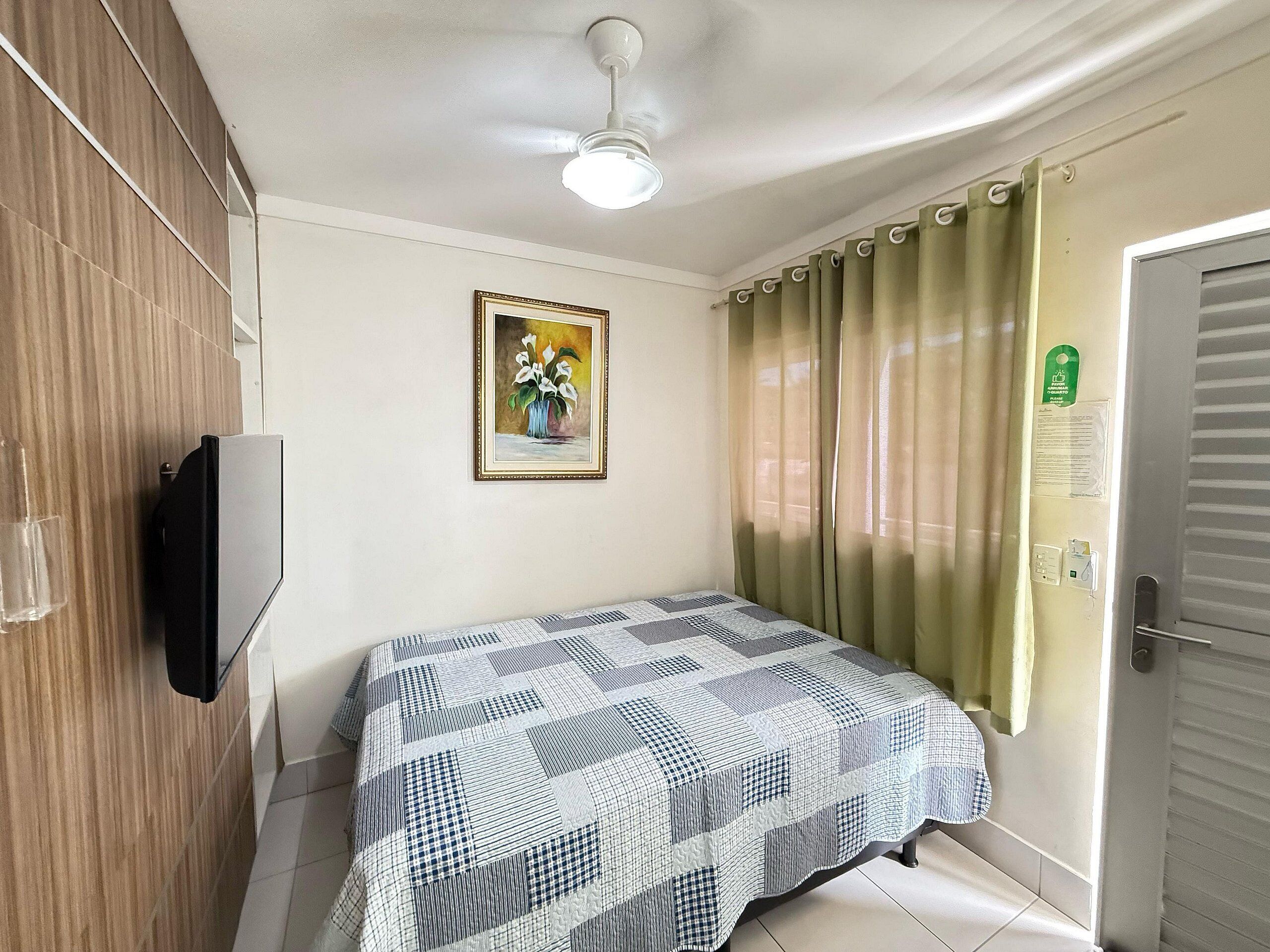 Ein Schlafzimmer mit Bett, Deckenventilator, einem Gemälde, Vorhängen und einer Tür.