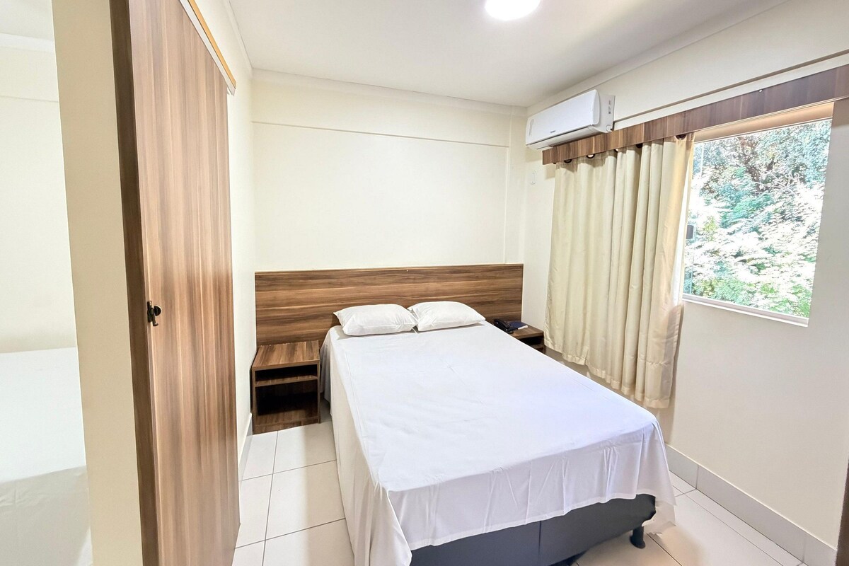 Una habitación de hotel con cama, mesita de noche y unidad de aire acondicionado.