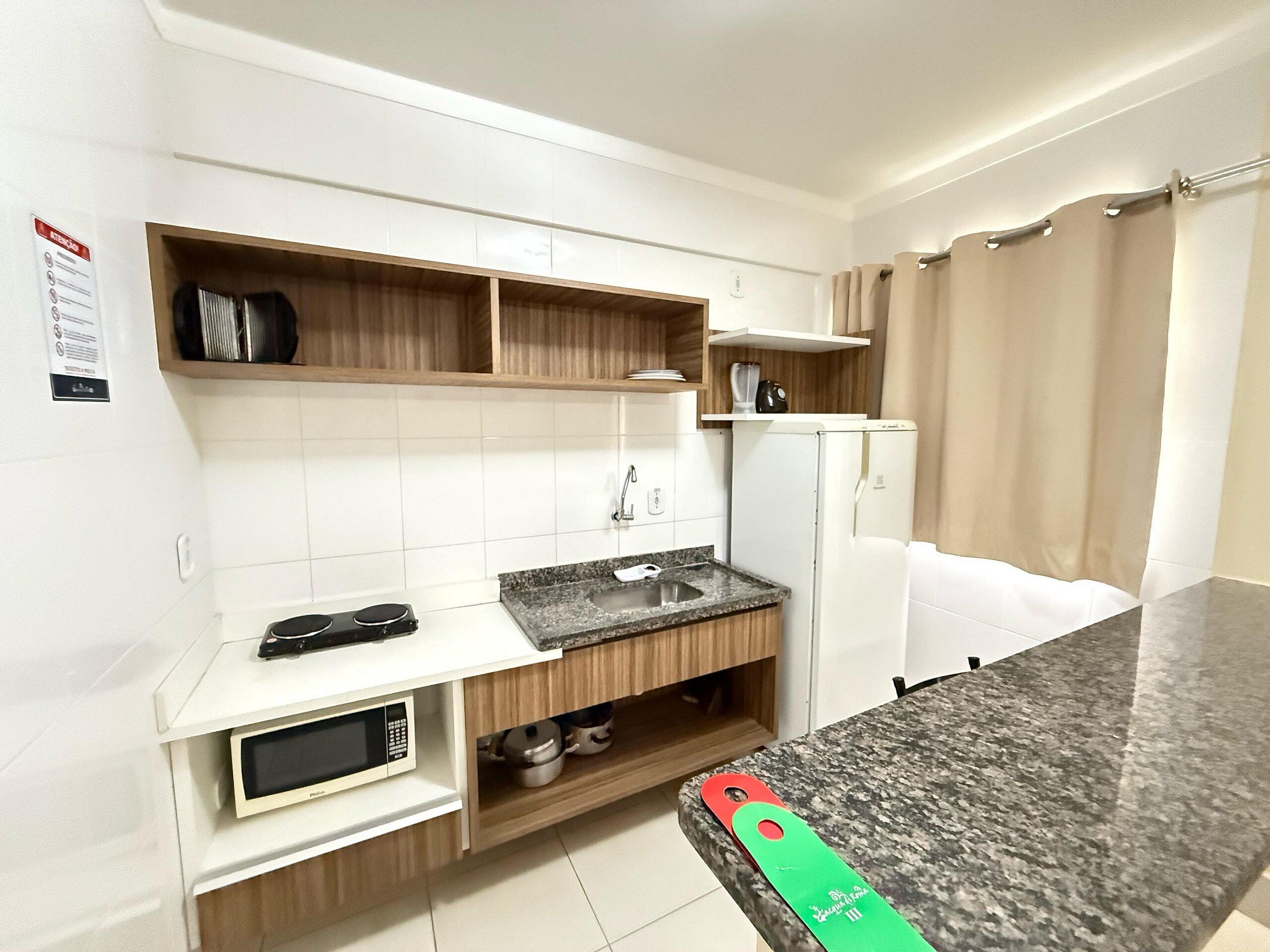 A compact kitchen with white cabinets, a granite countertop, a microwave, a sink, and a refrigerator.