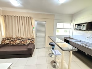 A compact living space with a sofa, a small bar stool, a kitchenette with a microwave, and a door with a curtain.