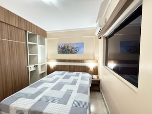 A bedroom with a bed, a painting of flowers, a wardrobe, and a window.