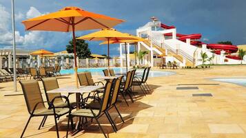 A poolside area with lounge chairs and tables, a pool, and a water slide structure.